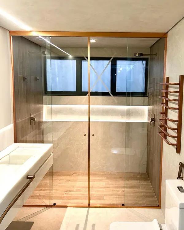 Box de vidro temperado do piso ao teto com perfis dourados em banheiro amplo