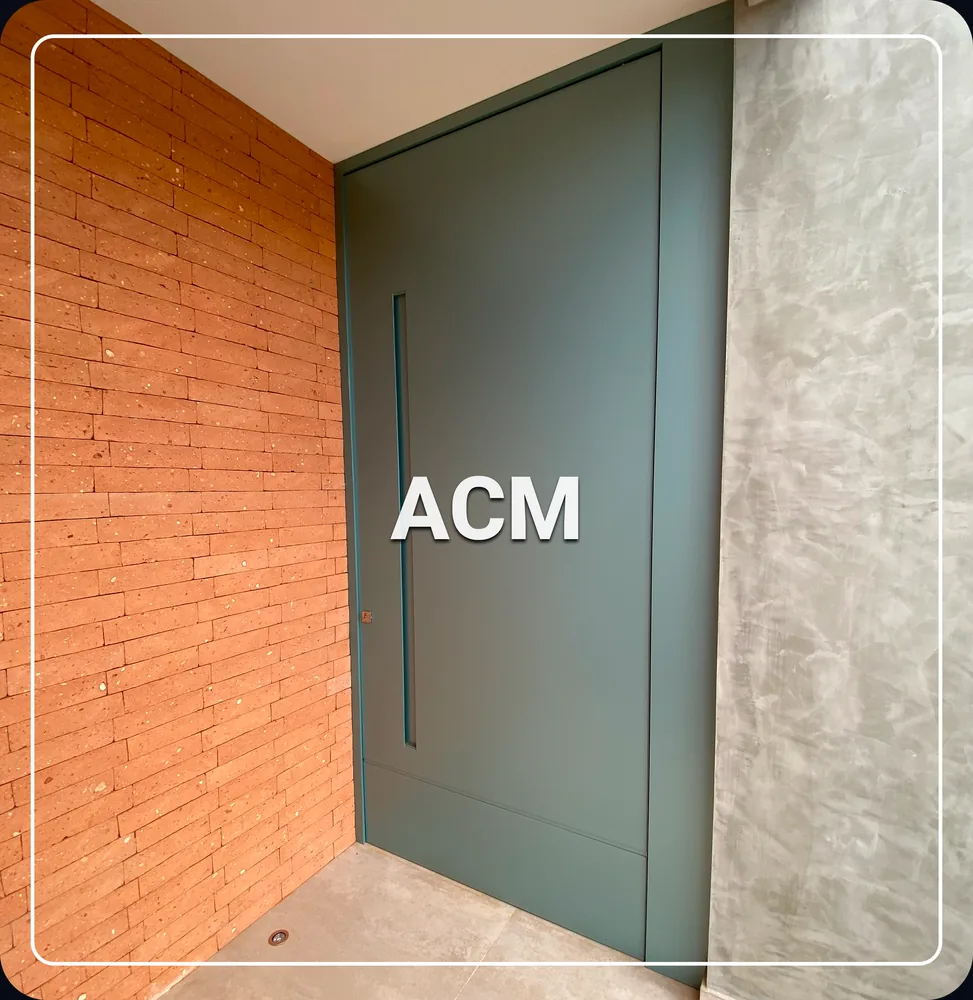 Porta pivotante em ACM verde da linha Velare instalada entre parede de tijolinho e cimento queimado