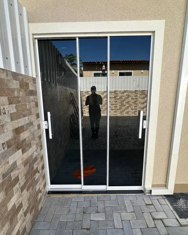 Porta de correr de vidro temperado com perfis brancos abrindo para área externa