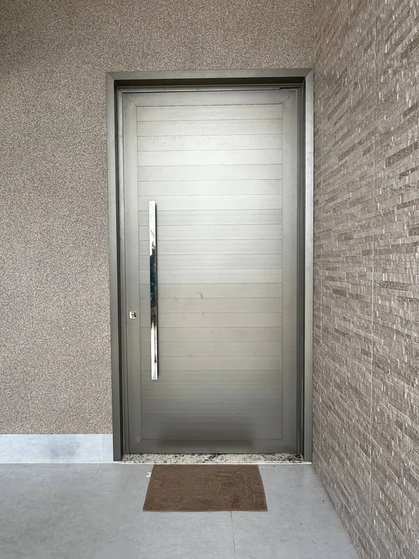 Porta pivotante em ACM com acabamento inox escovado e puxador vertical