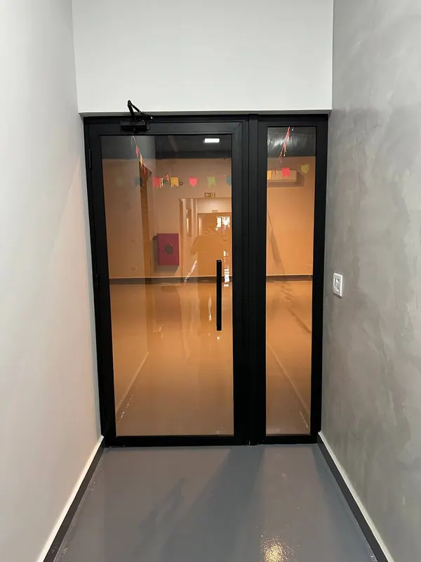 Porta dupla de vidro com perfis de alumínio preto em corredor interno